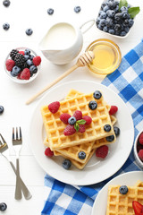 Sweet waffle with berries, milk and honey on white wooden table