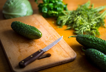 Fresh cucumbers, dill and parsley. Green vegetables on a wooden surface with knife.