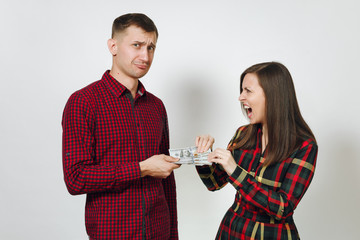 Pretty caucasian young couple. Angry indignant woman and surprised and dissatisfied man in plaid checkered clothes with cash dollars on white background isolated. Relationship, family, money concept.