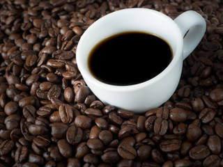 Roasted coffee beans with white cup of espresso.