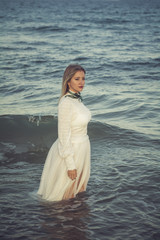 Young beautiful woman portrait, she has a white tulle dress and she is getting into the sea - Portrait of a poetic, vintage woman walking into the ocean, romantic mood