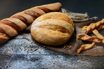 Close-up photo of composition of  bread on dark wooden table with flour around.