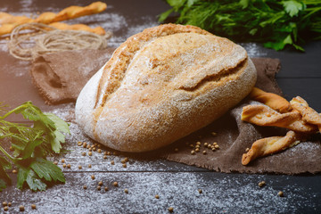 Close-up photo of composition of  white bread on dark wooden table with  greens around.