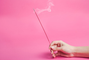 Obraz na płótnie Canvas Female hand holding incense sticks that smokes isolated on pink background