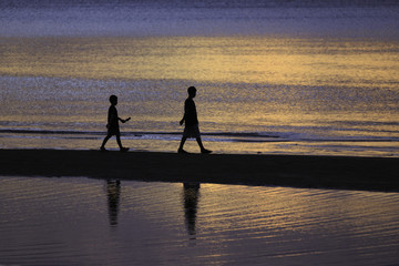 the silhouette photo of two brothers enjoy on the beach with colorful sea in sunrise