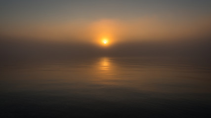 Red epic sunset over lake with reflection. Calm water and scenic sky merge together in mist.