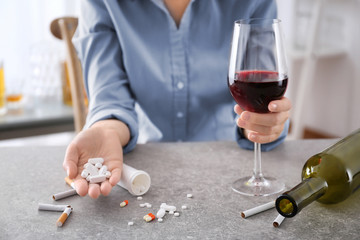 Young woman sitting at table with alcohol, pills and cigarettes. Concept of bad habits