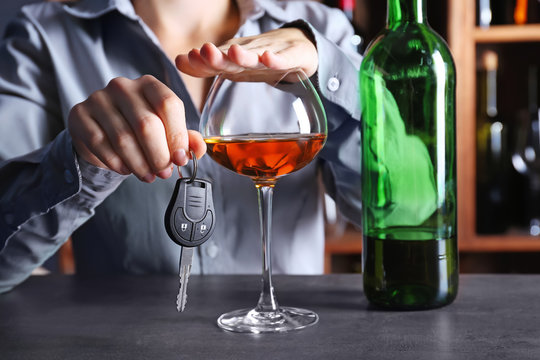 Woman covering glass of alcohol with hand while holding car key in bar. Don't drink and drive concept