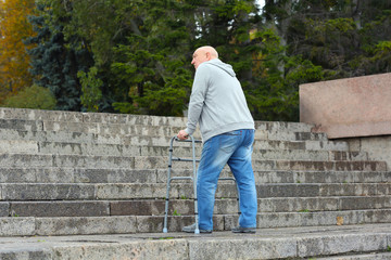 Fototapeta premium Elderly man with walking frame going up the stairs outdoors