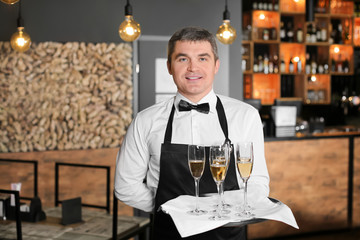 Waiter holding tray with glasses of champagne indoors