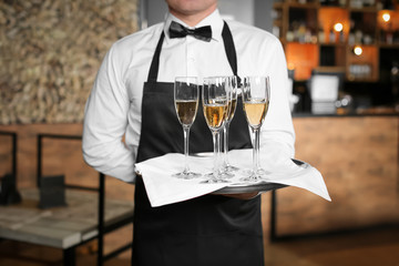 Waiter holding tray with glasses of champagne indoors