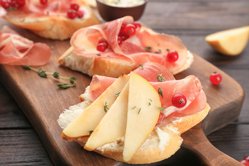 Tasty bruschetta with pear and prosciutto on wooden board, closeup