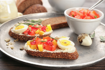 Tasty bruschettas with quail egg and vegetables on metal plate, closeup