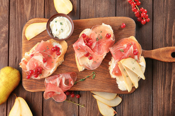 Tasty bruschettas with pear and prosciutto on wooden board, top view