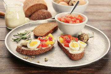 Tasty bruschettas with quail egg and vegetables on metal plate