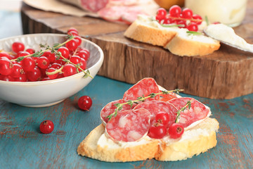 Tasty bruschetta with red currant and salami on table, closeup