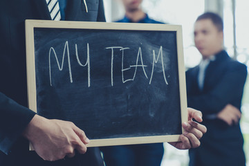 "My Team" wording on chalk blackboard in a hand of businessman in wearing black suit ; Business concept pic.