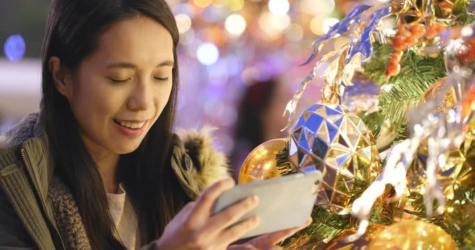 Woman taking photo on mobile phone on Christmas tree decoration at night
