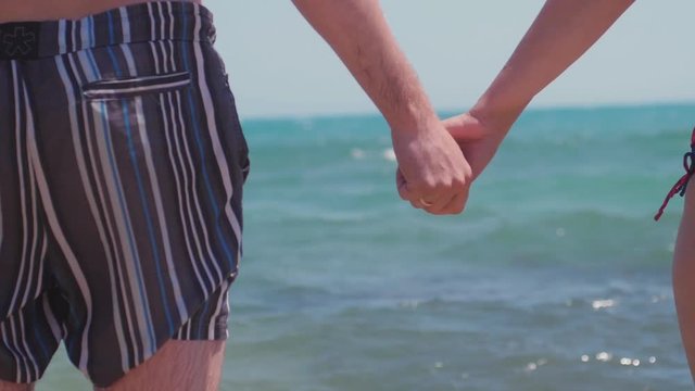 A young couple in love holding hands on the beach by the sea and splashing waves in slow motion. 1920x1080