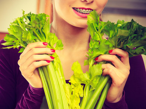 Woman in kitchen holds green celery