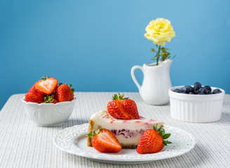 Delicious cheesecake with strawberry on a table against blue wall.