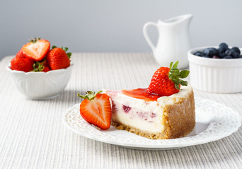 Delicious cheesecake with strawberry on a table against white wall.