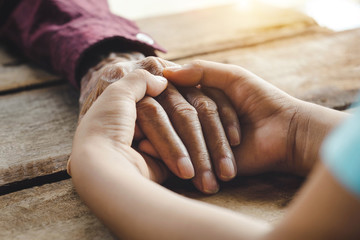 Hands of the old man and a child's hand on the wood table
