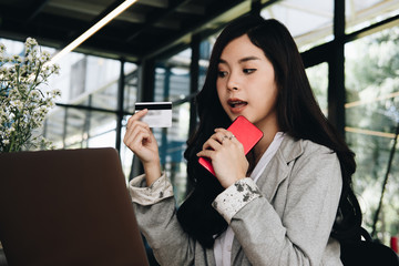 woman holding a credit card and using smart phone for online shopping at cafe. businesswoman purchase goods from internet at office. female adult make payment on bank website at workplace
