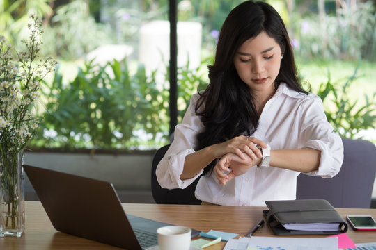 businesswoman look at her watch at workplace. startup woman check time on wristwatch at office.  young female entrepreneur with paperwork on table.