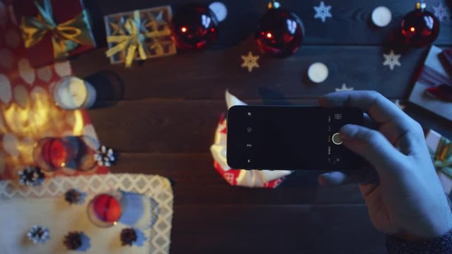 Man takes picture of his New Year present on smartphone camera on decorated Christmas table, top down shot