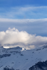Fototapeta na wymiar Snowy off-piste slope and sunlight mountains in clouds