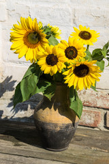 Sunflowers in vintage clay jug on wooden table