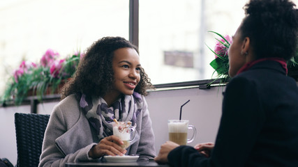 Two attractive mixed race women talking and drinking coffee in street cafe. Friends have fun after visiting mall sale