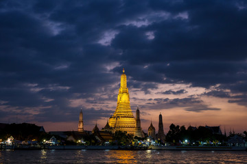 Naklejka premium Landscape image of temple of dawn or Wat Arun and Chao Phraya River in the front when the sunset at dusk time is beautiful with warm gold color tone.