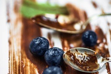 Blueberry, dirty spoon and mint leaf on dirty background with chocolate lines.