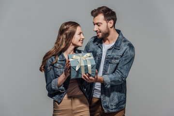 beautiful happy young couple holding gift box and smiling each other isolated on grey