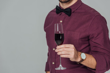 cropped shot of young man holding glass of red wine isolated on grey