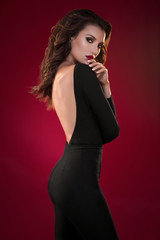 Woman in black dress on the red background posing at camera