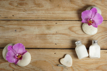 Body lotion and stones for a hot massage are spread out on a wooden table before the spa procedure. Ornament of beautiful orchid flowers.