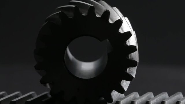 Rotating helical gear rack and a pinion on black background