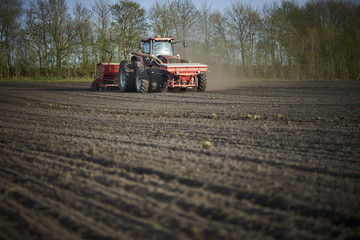 Fototapeta premium Red tractor with sowing machine on a ploughed field