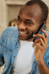 Nice talk. Attractive inspired young afro-american man grinning and talking over the phone and looking in the distance