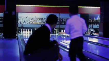 Little boy try to play a game of bowling with father. Kid rolling ball and has fault. Child don't have experience in game. Wrong way. Goal not achieved