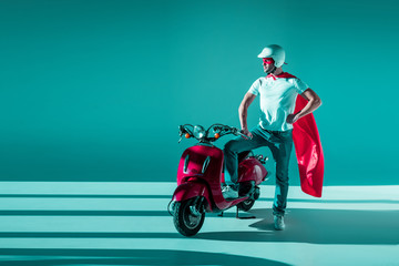 man in protective helmet, superhero mask and cape standing at red scooter