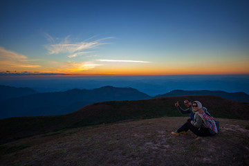 Fototapeta premium couples of man and woman sitting on top of mountain scene with beautiful sunset sky on high mountain
