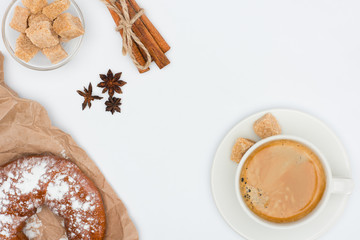 top view of cup of coffee with saucer and brown sugar, pastry, anise stars and cinnamon sticks tied with rope isolated on white