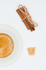 top view of cup of coffee with saucer, brown sugar and cinnamon sticks with rope isolated on white