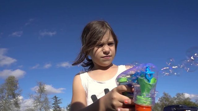 Happy 6 year old girl with bubble gun shooting soap bubbles outdoors Slow motion