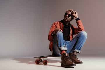 Stylish young african american skateboarder sitting on longboard © LIGHTFIELD STUDIOS