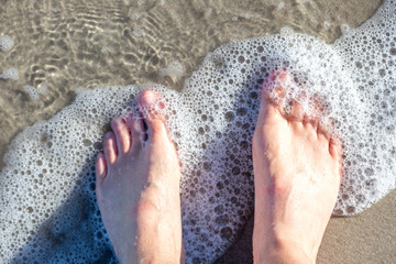 Füße werden am Strand von Wellen umspült